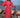 Woman in a red dress standing next to a motorcycle by the ocean in lombok indonesia.  wearing a broderie anglaise kaftan in bright red cherry colour, and pure silk headband with custom artwork. 