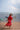 Woman in a red dress walking on a beach with boats in the background