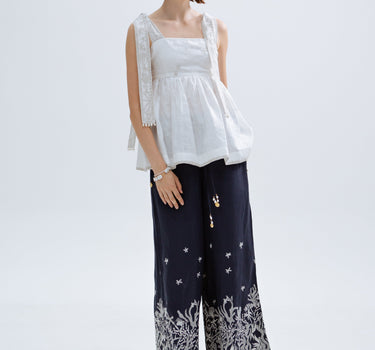 Woman wearing a white top and navy embroidered pants on a white background