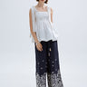 Woman wearing a white top and navy embroidered pants on a white background