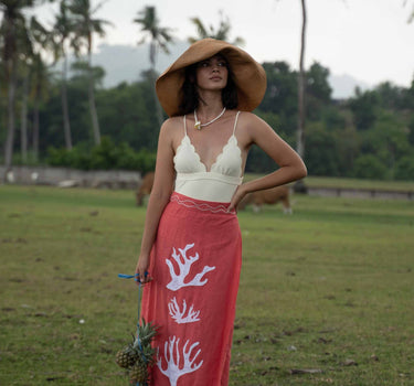 The Poseidon Wrap Skirt is a classic full-wrap style, below knee length, featuring extra long ties, and stunning applique and embroidery details on coral red linen. 
 The contrasting ivory applique features our signature coral motif, with glass pearl beads, and each tie features real natural baroque pearl charms at each end. Design by Fleur Kakasi